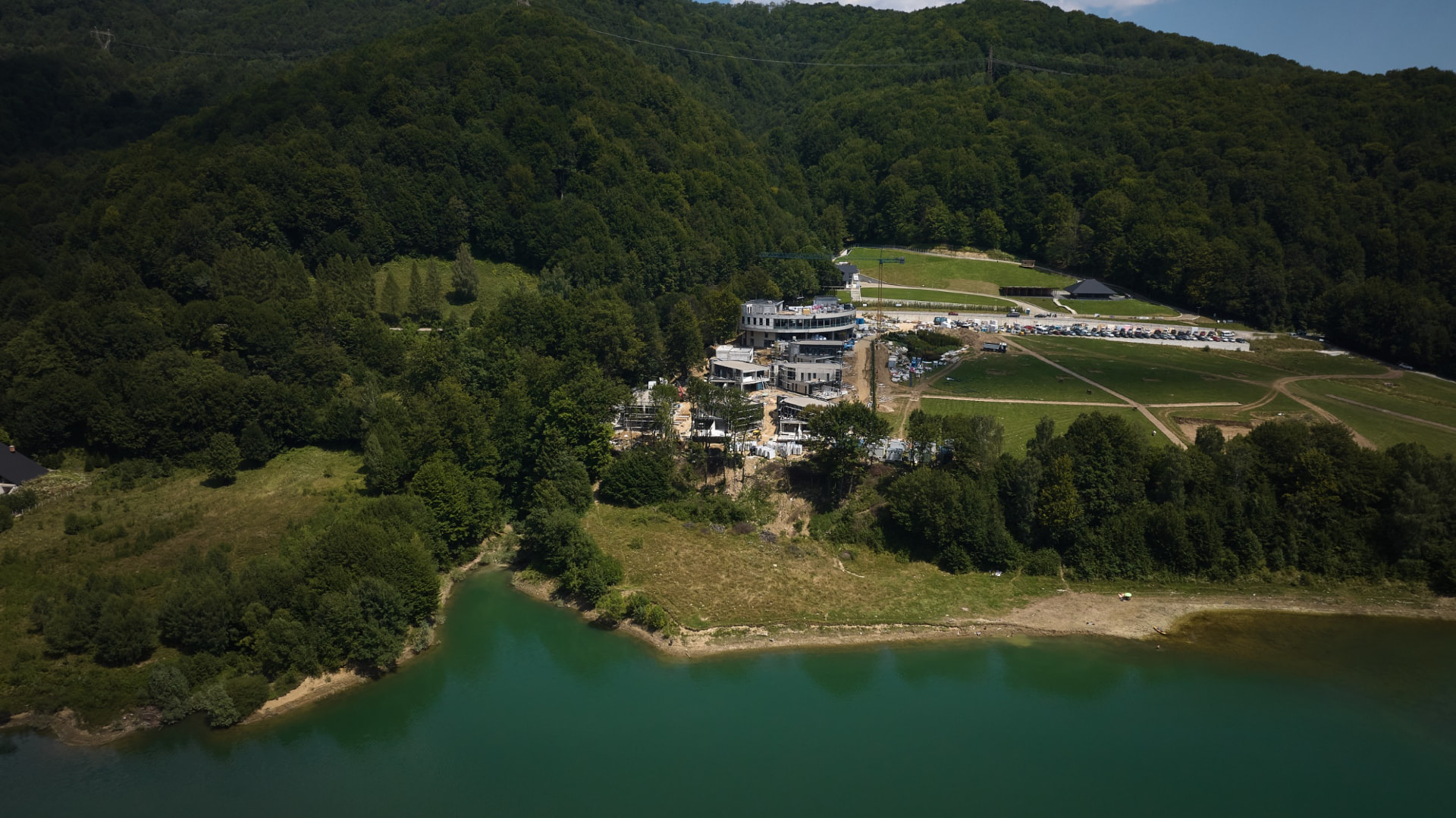 Resortul în construcție pe malul lacului, înconjurat de pădure