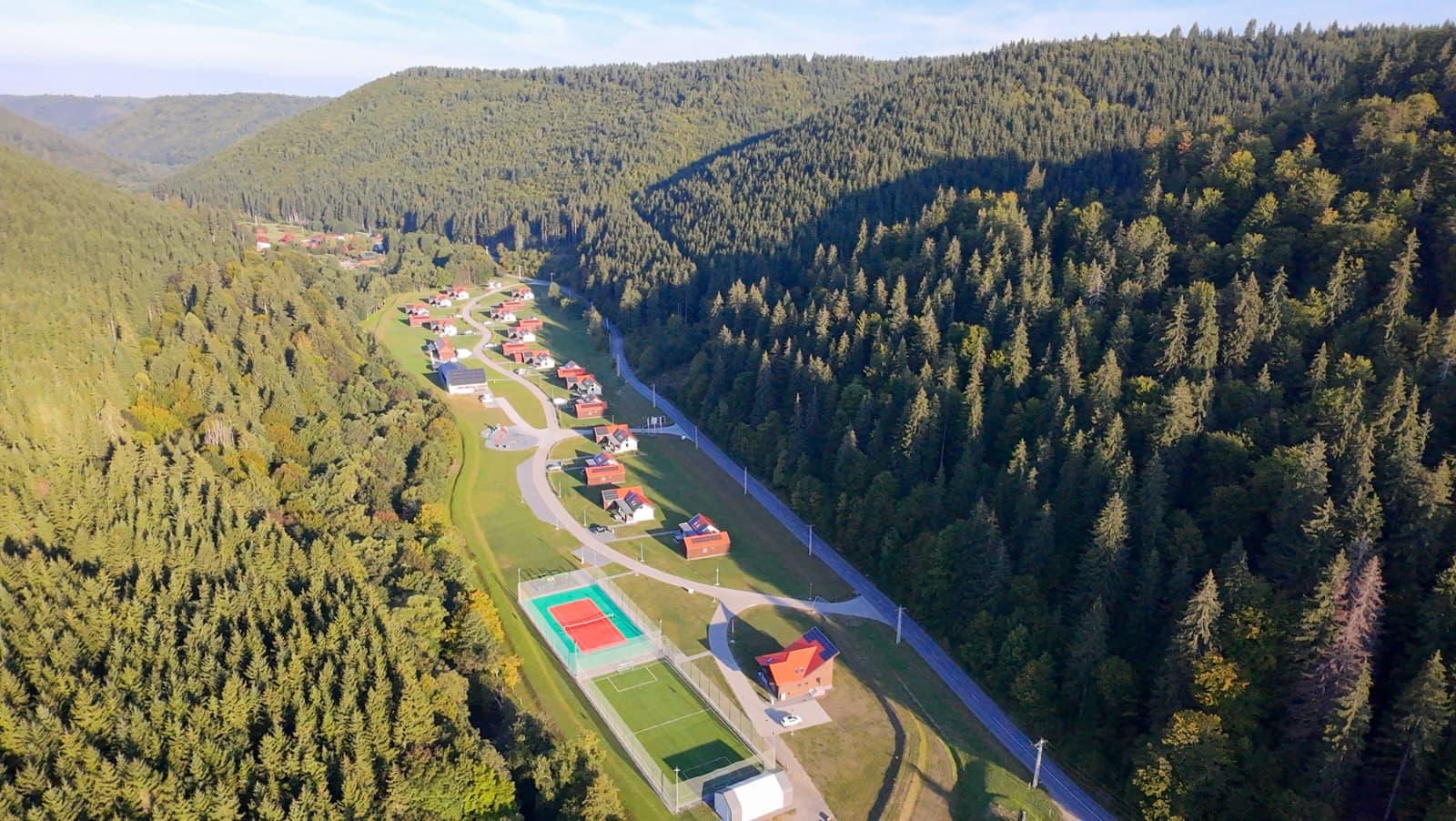 Vedere aeriană a resortului Eskaperdo și a terenurilor de sport, între dealuri împădurite