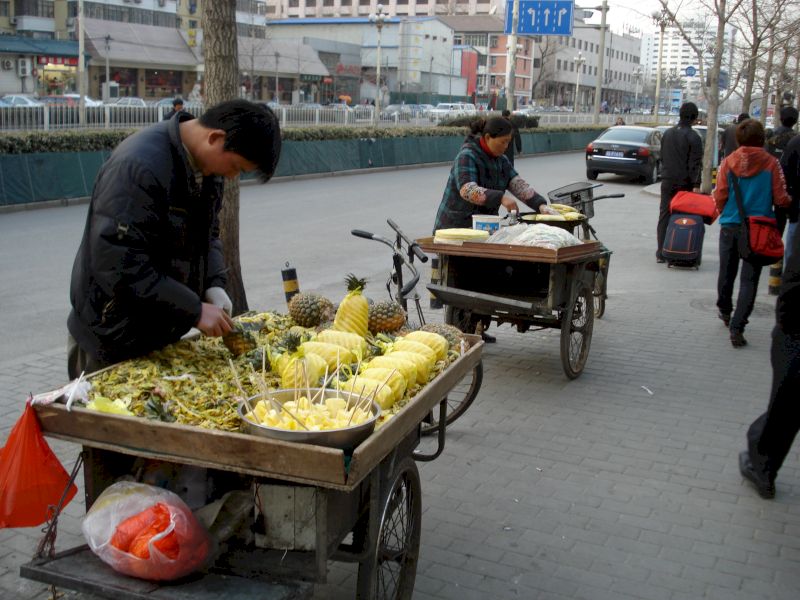 Vânzător tăind ananas la un cărucior pe trotuar