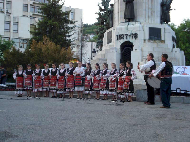 Grup în costume populare aliniat în fața unui monument