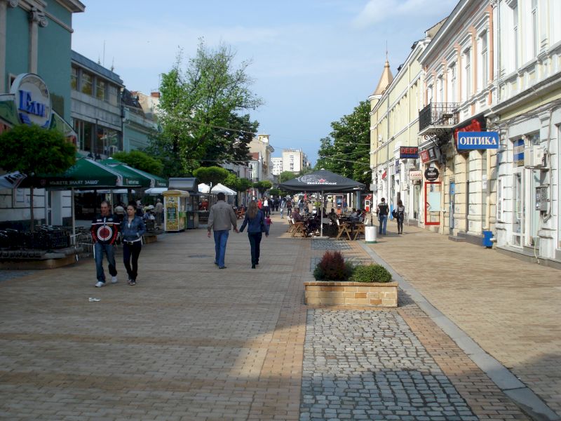 Pietoni pe stradă pavată între clădiri și terase