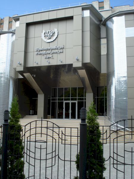 Intrare monumentală gri cu emblemă deasupra unei porți metalice