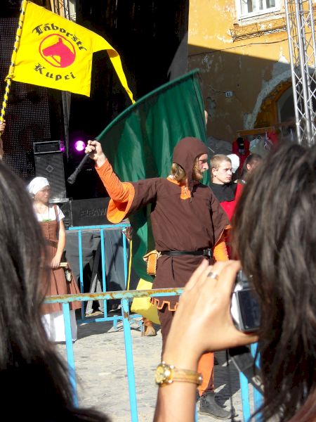 Persoană costumată ridicând brațele lângă un steag galben
