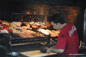 Coca Cola Montevideo Bărbat cu tricou roșu lângă un grătar încărcat cu carne