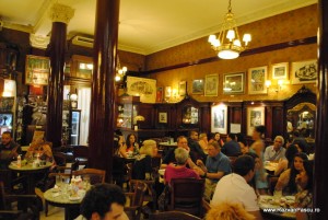 Cafenea aglomerată cu coloane, tablouri și candelabre aprinse