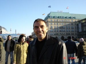 Dragos Anastasiu Bărbat zâmbitor într-o piață cu trecători și clădire monumentală