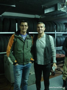Doi bărbați zâmbind lângă un perete cu anvelope stivuite