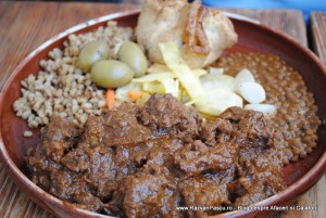 Farfurie brună cu carne în sos, cereale, ceapă și pâine.