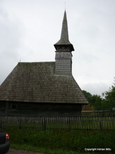 biserica_de_lemn_din_cupseni Biserică din lemn închis la culoare, cu acoperiș înalt și turlă ascuțită.