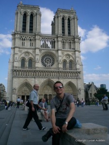 1-Notre_Dame_resize Bărbat în fața unei catedrale gotice cu două turnuri și rozasă.