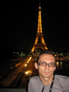 13_-_Inafara_Tour_Eiffel_resize Bărbat cu ochelari, cu Turnul Eiffel iluminat în spate noaptea.