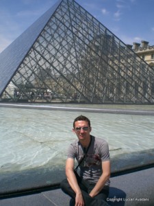 7-Piramida_Louvre Bărbat așezat lângă bazin, în fața piramidei de sticlă.