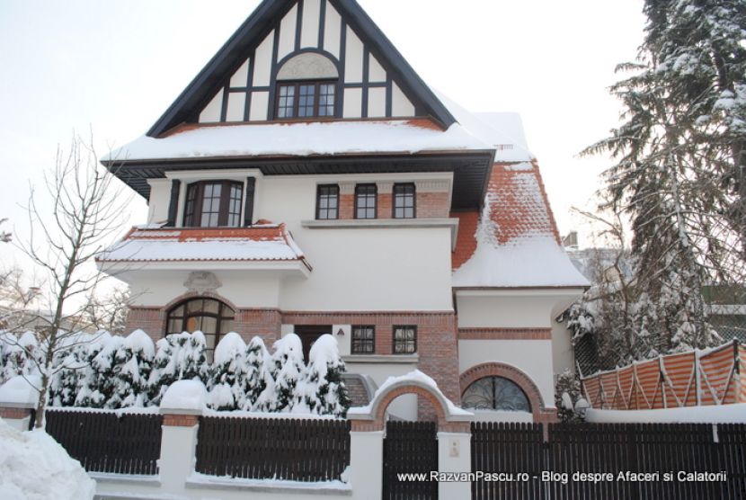 Vilă cu fronton triunghiular și grinzi decorative negre, sub un acoperiș înzăpezit.