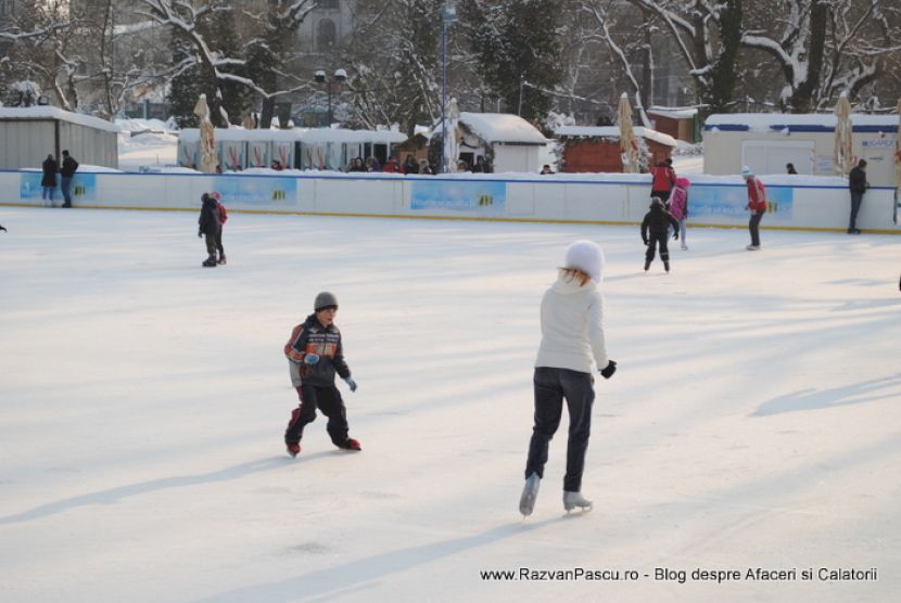 Patinatori răsfirați pe gheață, cu o persoană în pulover alb în prim-plan.
