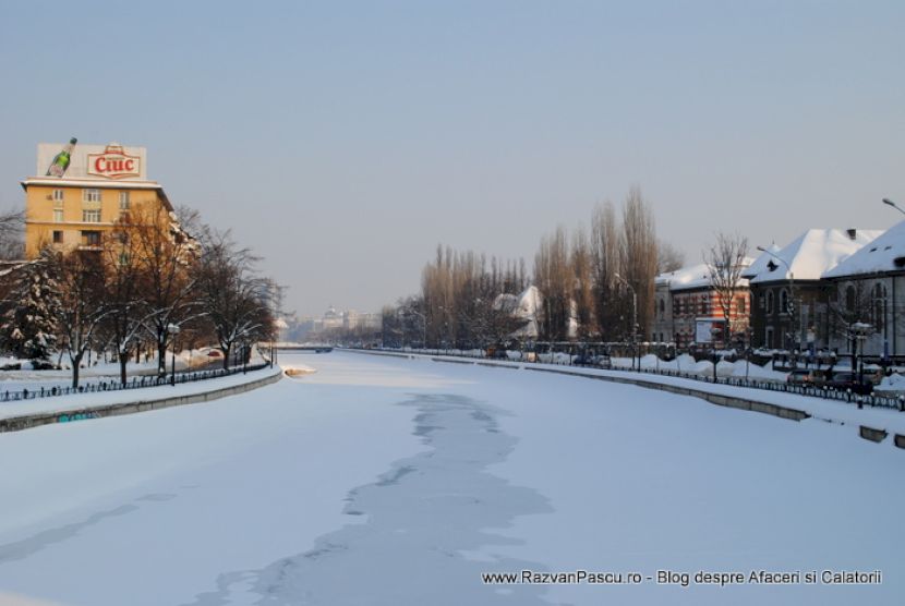 Albie înzăpezită între maluri urbane, cu o urmă sinuoasă pe suprafața albă.