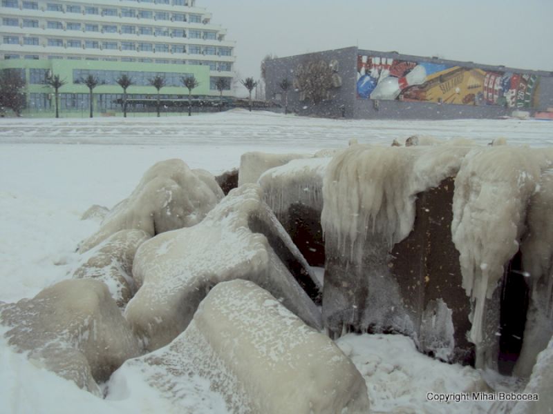 Blocuri înalte cu țurțuri masivi, în fața unei clădiri cu pictură murală.
