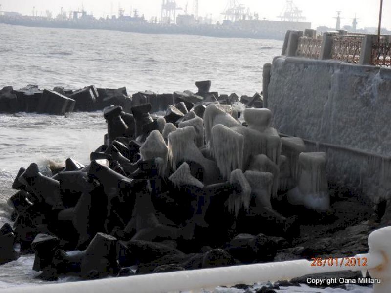 Blocuri de protecție din beton, parțial înghețate, lângă zidul de la mare.