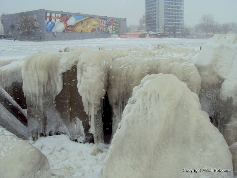 Structuri masive acoperite cu perdele de gheață, cu clădiri urbane în spate.