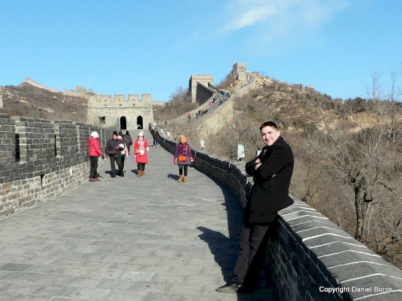 Bărbat lângă parapetul unui zid fortificat, cu turiști și dealuri în fundal.