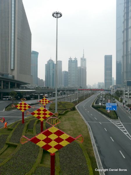 Bulevard aproape gol printre turnuri, lângă un rond decorat roșu și galben.