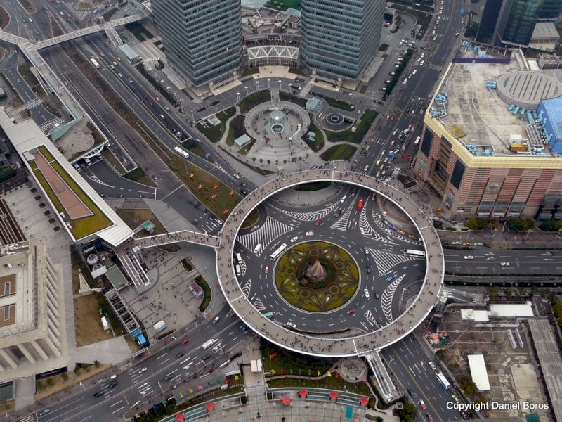 Intersecție cu sens giratoriu și pasarele circulare, văzută de sus între clădiri.