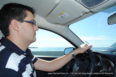 masina 1 Bărbat cu ochelari conduce un automobil, cu marea vizibilă pe geamul lateral.
