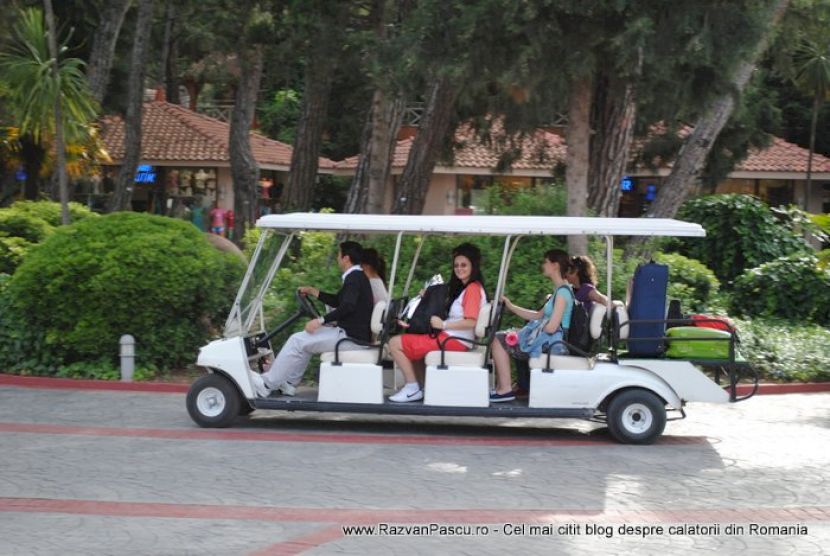 Pasageri într-un vehicul electric alb, pe aleea unui complex hotelier.