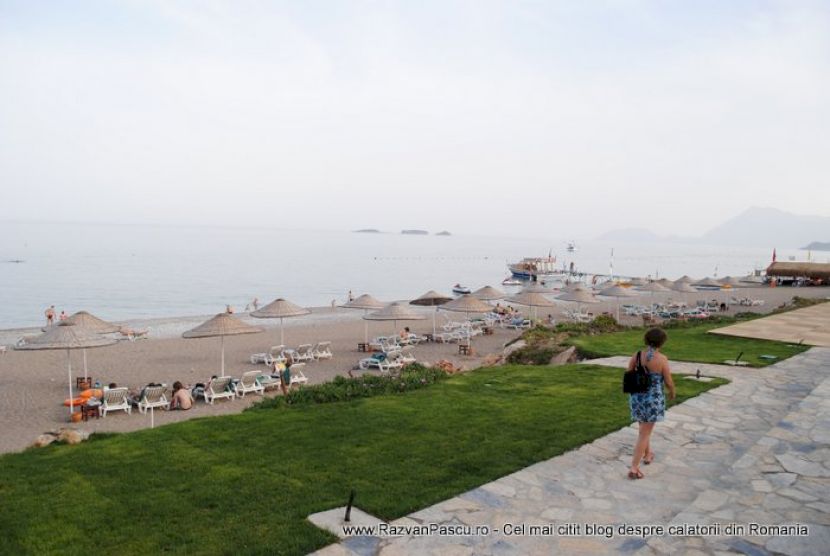 Plajă cu umbrele, văzută de pe aleea mărginită de gazon.