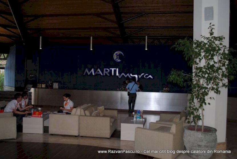 Recepție hotelieră cu canapele bej și siglă pe peretele albastru.