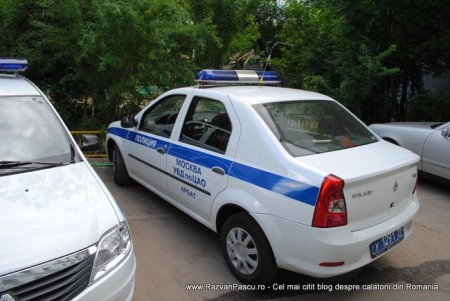 11 masini de politie Mașină albă de poliție cu bandă albastră, parcată lângă copaci.