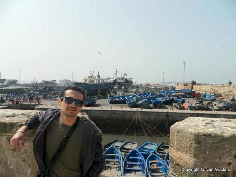 Turist lângă un parapet, cu bărci albastre în port.