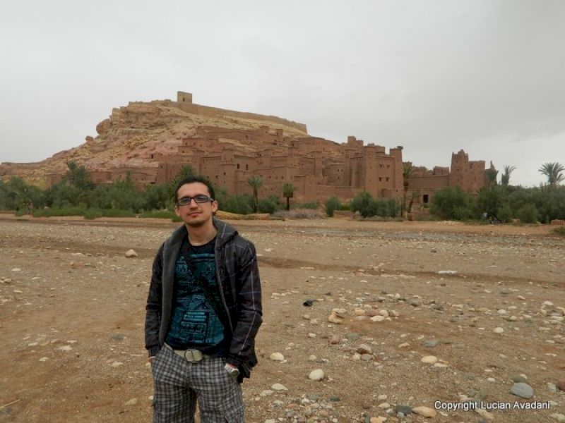Turist în jachetă închisă, cu așezarea fortificată pe deal în fundal.