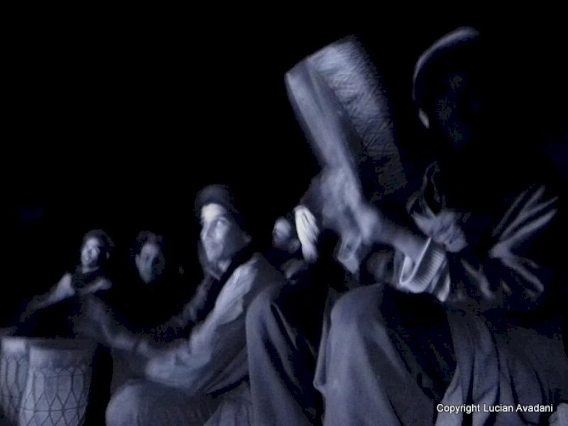 Oameni așezați în întuneric, unul ținând un instrument de percuție.