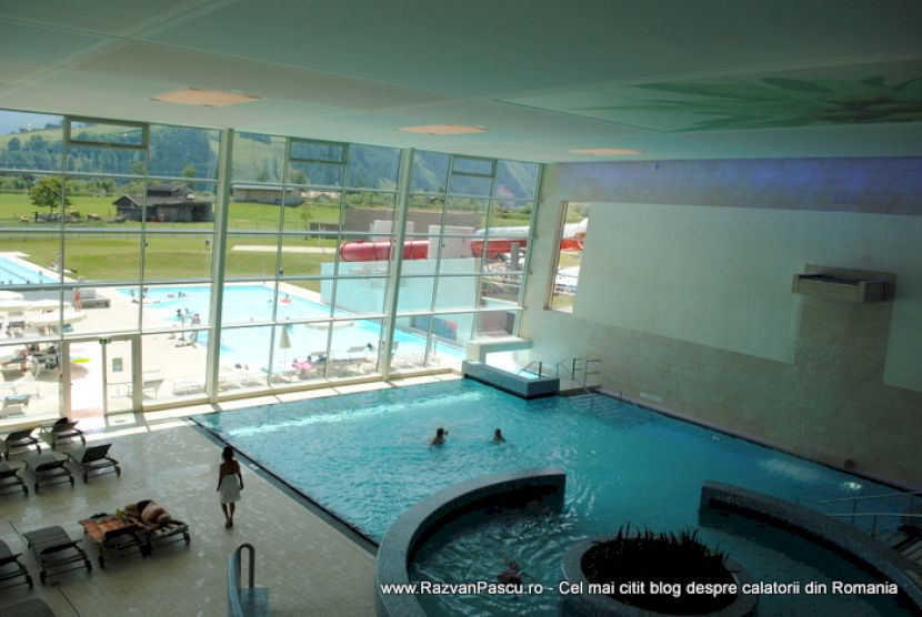 Bazin interior cu margine curbată și ferestre spre piscinele exterioare.