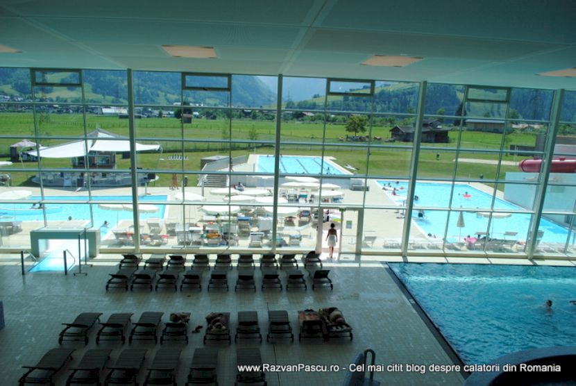 Vedere de sus asupra șezlongurilor interioare și piscinelor dincolo de geamuri.
