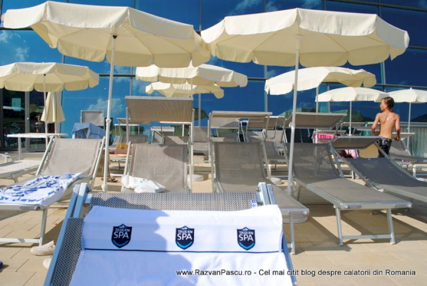 Șezlonguri cu prosoape albe, sub umbrele crem lângă piscină.