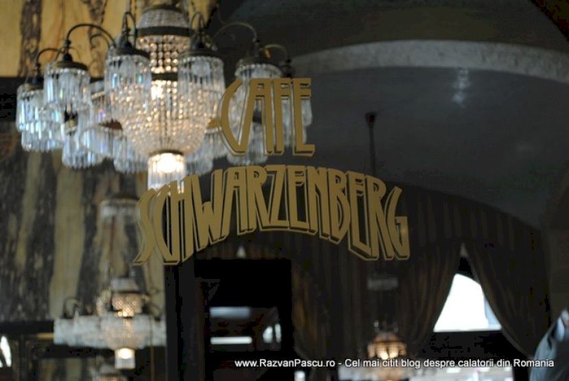 Inscripție aurie Café Schwarzenberg pe geam, cu candelabre reflectate.