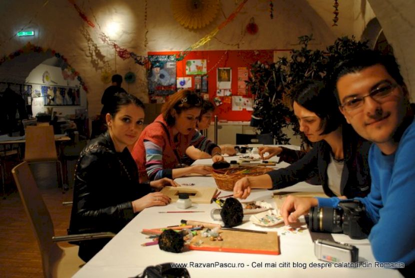 Participanți așezați de-a lungul mesei de atelier, cu lucrări în față.