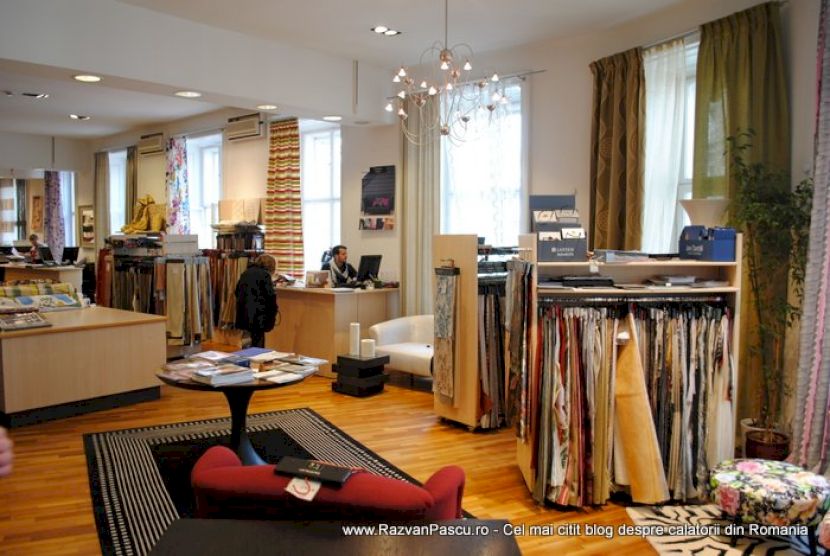 Showroom cu mostre textile suspendate, mese de lucru și ferestre înalte.