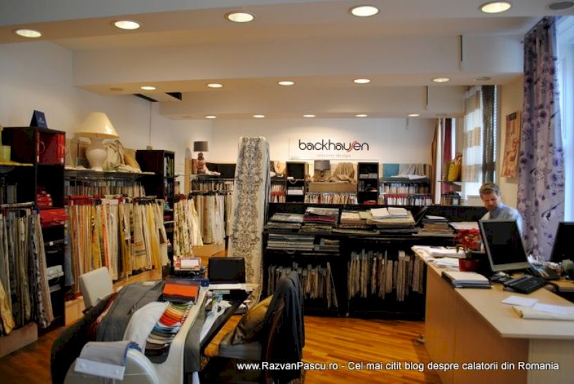 Magazin luminos cu rafturi și standuri pline de mostre textile.