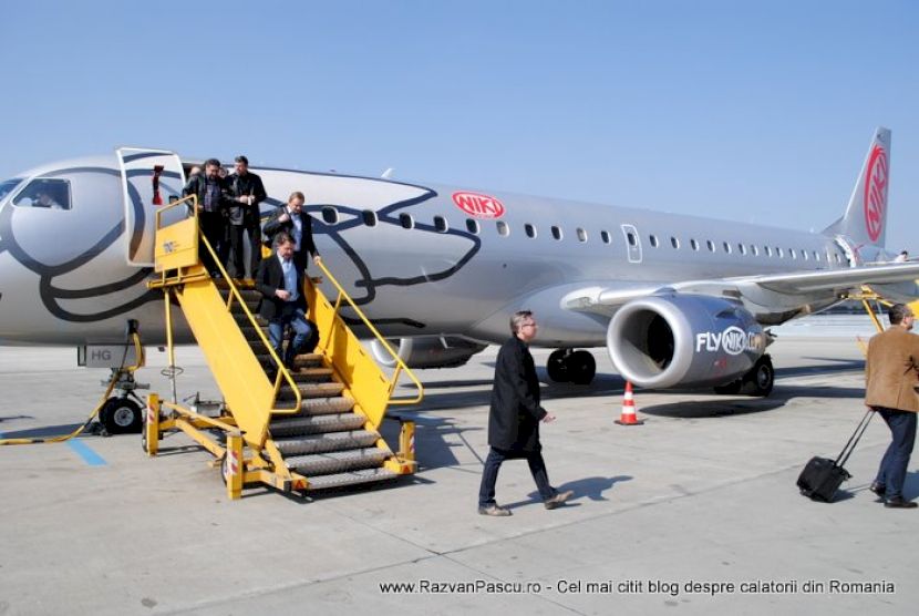 Pasageri coboară pe scara galbenă a unui avion parcat pe platformă.