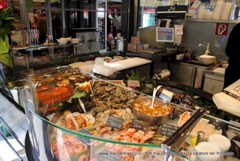 Salate și preparate variate într-o vitrină, lângă cântarul de pe tejghea.