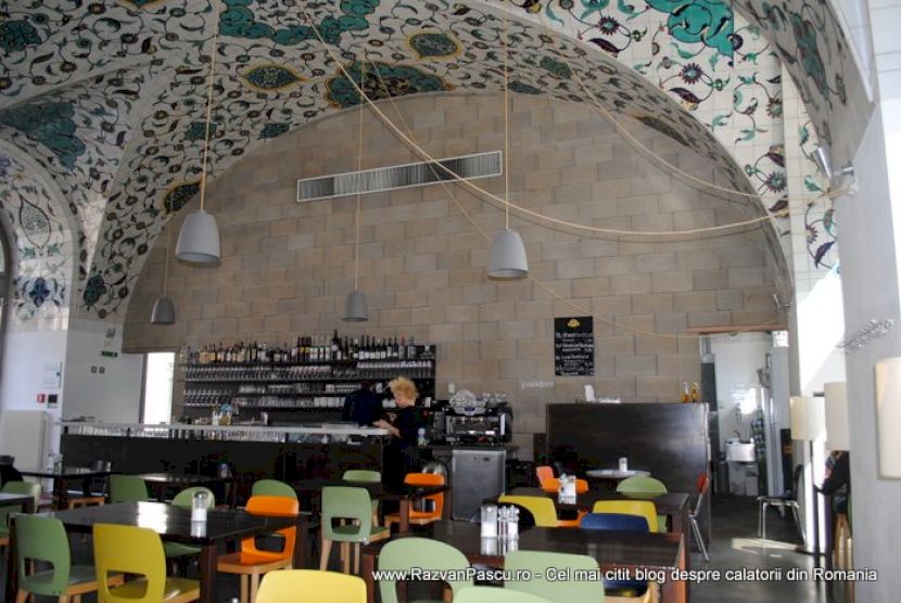 Restaurant cu scaune colorate, sub o boltă decorată cu mozaic.