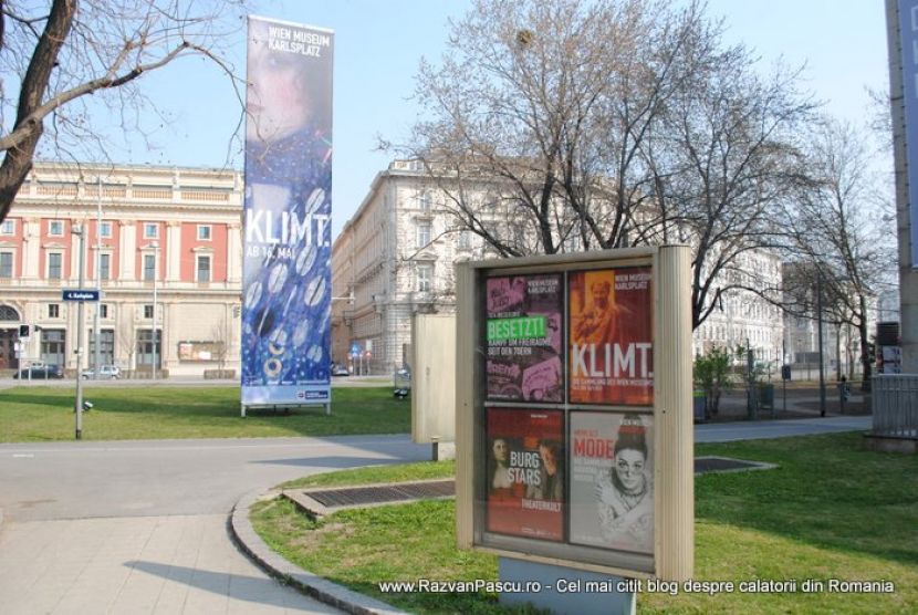 Panouri expoziționale despre Klimt, amplasate într-un parc cu arbori fără frunze.