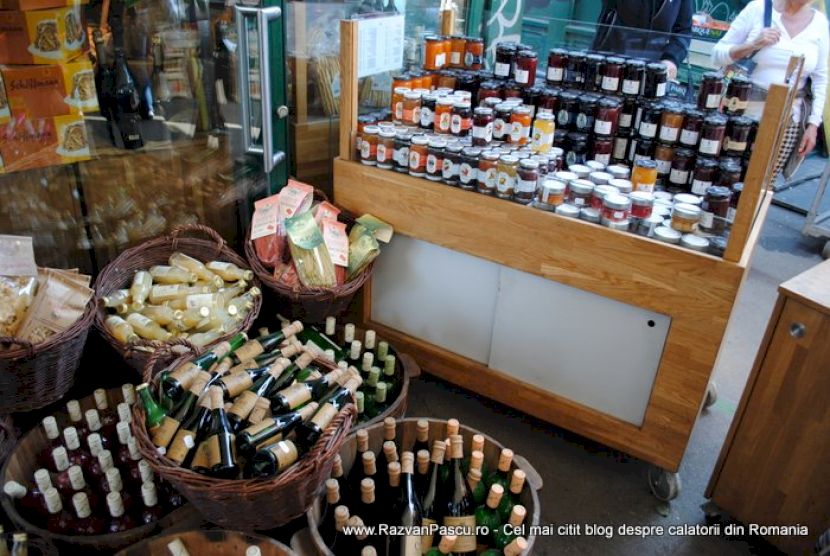 Sticle de vin în coșuri, lângă borcane aliniate pe tejghea.