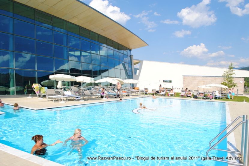 Piscină exterioară lângă o clădire cu fațadă albastră din sticlă.
