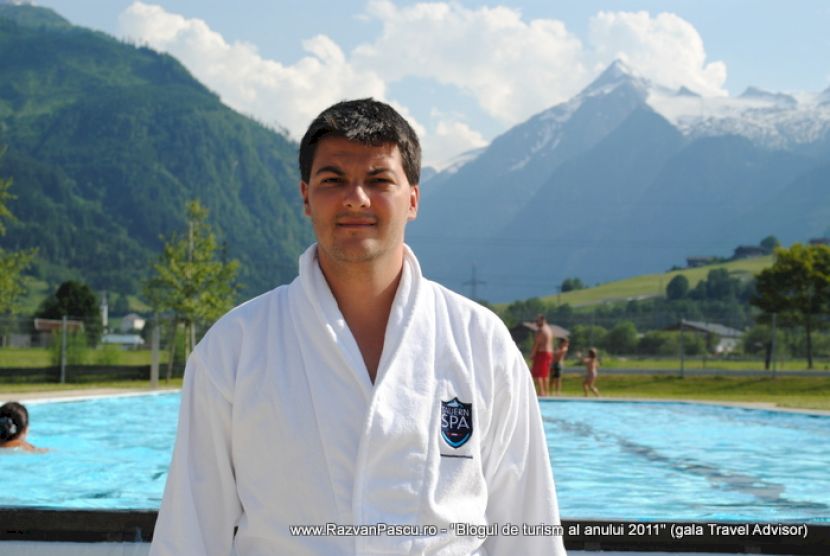 Bărbat în halat alb lângă piscină, cu munți în fundal.