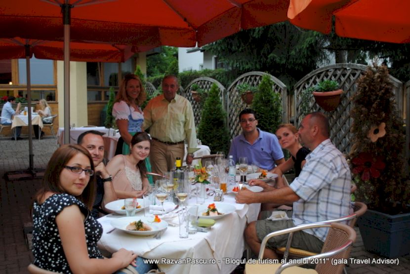 Grup la o masă în aer liber, sub umbrele portocalii.