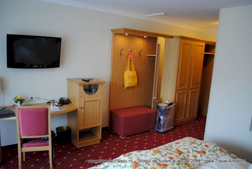 Cameră de hotel cu televizor pe perete și dulap deschis.