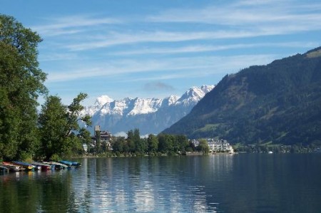 Lac liniștit cu munți înzăpeziți în depărtare și arbori pe mal.
